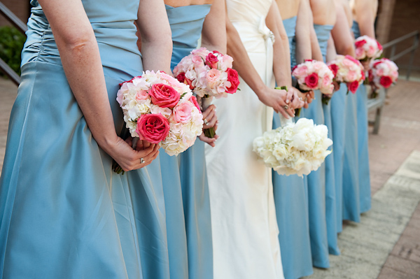 bride and bridesmaids holding bouquets behind their backs - bride in white is holding ivory bouquet and bridesmaids in light blue are holding dark pink, light pink, and ivory bouquets - photo by Houston based wedding photographer Adam Nyholt